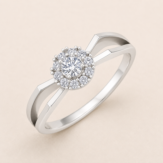 A silver-toned halo ring with a round-cut center stone and a surrounding halo of smaller stones, shown on a soft beige background.