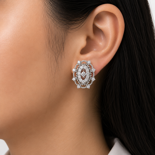 A close-up of a model's ear wearing a detailed oval stud diamond earrings with a silver-toned metal setting, clear pavé diamond , and a central diamond .