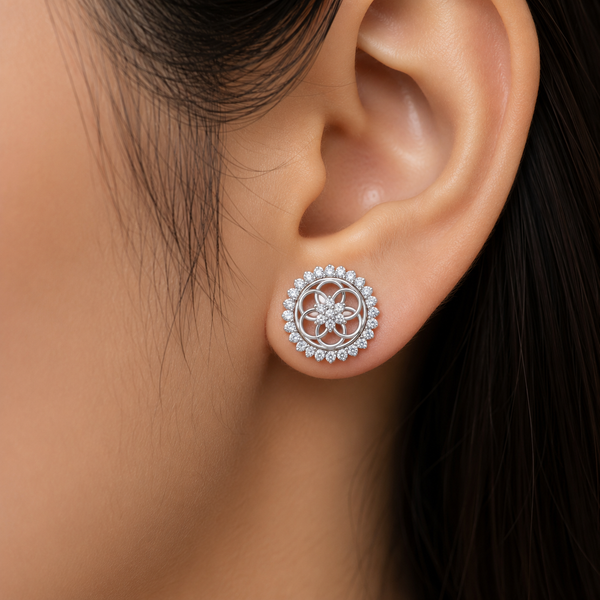 A close-up of a woman's ear wearing a round silver-toned stud earring with a floral mandala design surrounded by small clear diamonds.