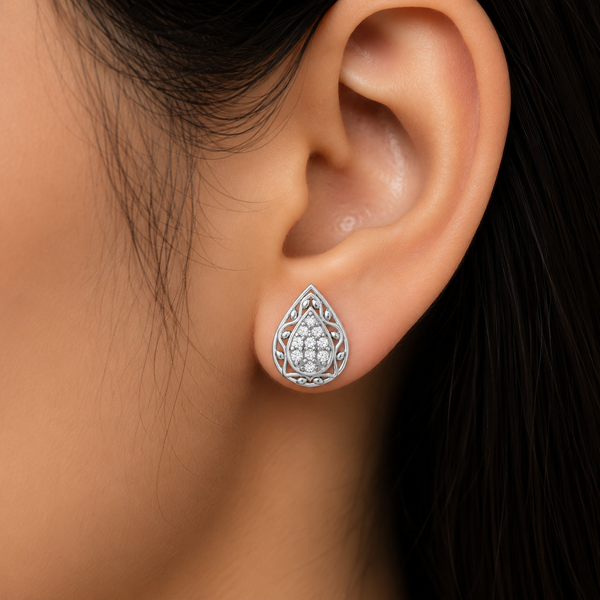 A close-up of a person's ear wearing a teardrop-shaped silver stud diamonds earring with intricate filigree detailing and a central cluster of small clear diamonds.