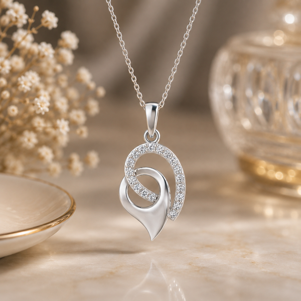 A silver pendant diamond necklace with interlocking curved heart and crescent motifs, one adorned with small clear diamond , displayed on a warm beige surface with soft decorative props in the background.
