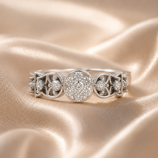 A silver three-stone ring featuring a central round cluster of clear stones flanked by two smaller matching clusters, displayed on a draped champagne satin fabric.