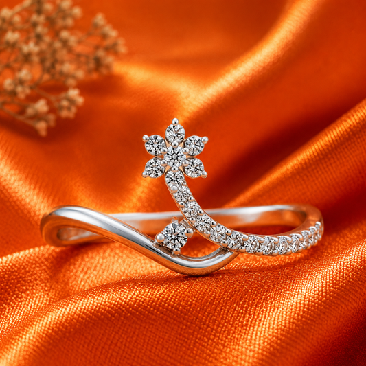 A silver-toned ring with a curved band and a flower-shaped cluster of clear stones, displayed on draped orange satin fabric.