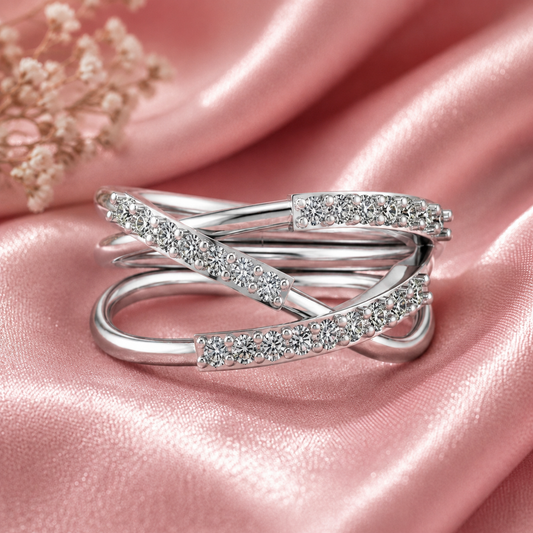 A silver-toned wrap ring with pavé-set clear stones, displayed on a soft pink satin fabric background.