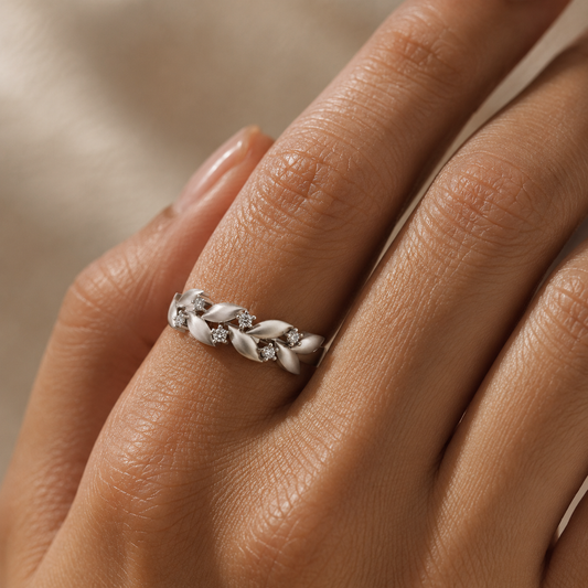 A silver ring with a braided leaf design and small clear stones, shown worn on a person's finger.