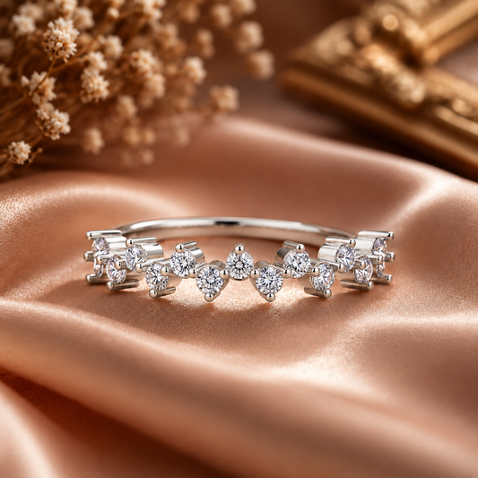 A silver-toned diamond band ring with a row of marquise-cut diamonds, displayed on draped champagne satin fabric with dried flowers in the background.
