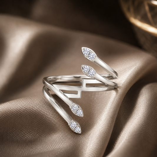 A silver wrap ring with three marquise-shaped diamond clusters, displayed on draped champagne-colored satin fabric.