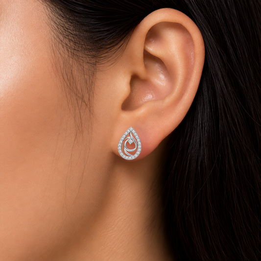 A close-up of a person's ear wearing a teardrop-shaped stud diamond  earring with a silver-tone double-ring design set with small clear diamond .