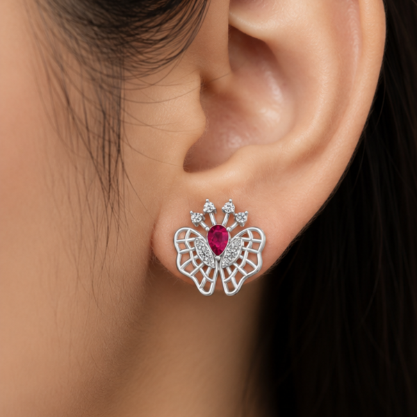 A close-up of a person's ear wearing a butterfly-shaped stud earring. The earring features silver-toned butterfly wings with a central teardrop-shaped pink gemstone and small clear Diamond at the top.
