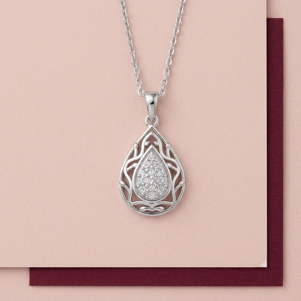 A silver teardrop diamond pendant necklace with an intricate filigree design and a sparkling clear diamonds center, displayed on a light pink card over a dark burgundy surface.