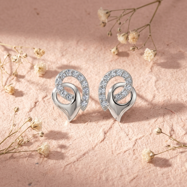 A pair of silver-toned spiral stud diamond earrings with clear pavé-set diamond , displayed on a textured pink surface with dried baby's breath flowers.