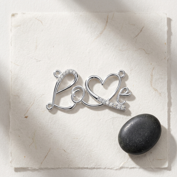 A silver-toned metal charm spelling 'Love' with a heart, displayed on a textured white paper background next to a smooth dark stone.